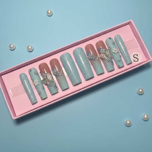 Set of decorative blue press-on nails in a pink box on a light blue background