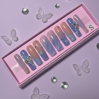 Set of colorful press-on nails with decorations in a pink box with butterflies and rhinestones on a purple background.