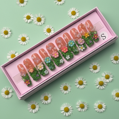 Set of decorative false nails with floral designs in a pink box, surrounded by daisies on a green background.